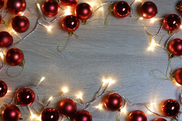 New year christmas frame from red shiny and matte balls, christmas lights garland on light wood background with copy space