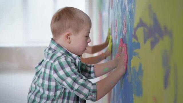 art kids paint in new home, boy with down syndrome and girl with paint on palms puts a hands on a colored wall during renovation