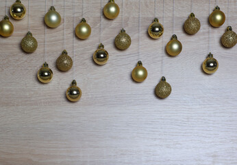 Golden christmas balls hanging on threads on light oak wood background. New year and christmas composition. Copy space