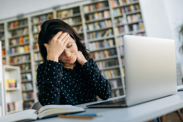 Headache while working. Stress. Young caucasian woman, manager or student, upset and tired from work sits at the desk, holding her head