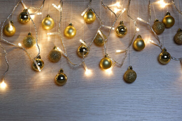 Golden christmas balls hanging on threads and garland of christmas lights on light oak wood background. New year and christmas composition. Copy space