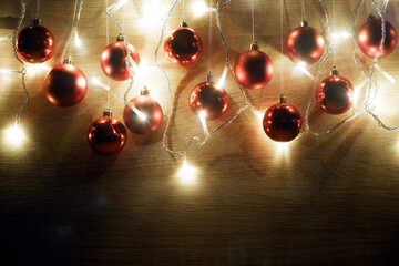 Red christmas balls hanging on threads and garland of christmas lights on light oak wood background. New year and christmas composition. Copy space