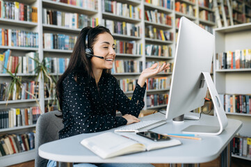 Caucasian smiling young woman call center worker, teacher or manager, wearing  a headset talking on video call with colleagues or clients, gesturing with hands while sitting at .
