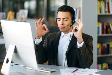 Keep calm! Hispanic successful young man, call center worker, manager or business man meditates...