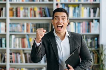 Emotional portrait of attractive hispanic man rejoicing over win or good news while looking straight at camera, indoors