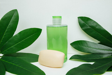 Cosmetic tonic in plastic bottle and soap on white background with green leaves close-up with empty space for text, skin care concept, personal care, advertising product, template, spa and massage
