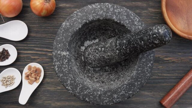 Top view of sea salt, brown sugar and peppercorns falling into the grey stone mortar in slow motion