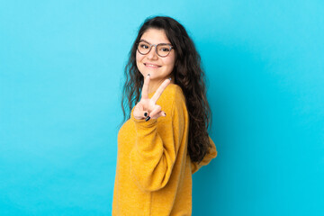 Teenager Russian girl isolated on blue background smiling and showing victory sign