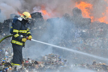 A fireman extinguishes huge landfill fire with flames and smoke in the background