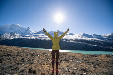 Successful woman trail runner open arms to beautiful landscape on high altitude winter sunrise lakeside
