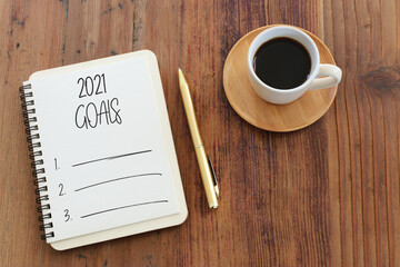Business concept of top view 2021 goals list with notebook, cup of coffee over wooden desk
