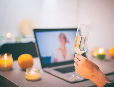 Close up of female hand with glass of champagne in front of laptop screen celebrating online video chatting