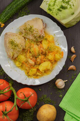 Chicken thighs with potatoes and carrots on a white round plate