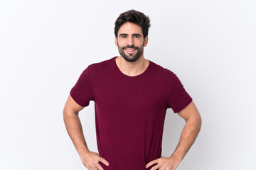 Obraz premium Young handsome man with beard over isolated white background posing with arms at hip and smiling