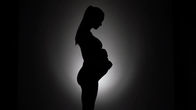 a silhouette of a pregnant woman standing and caressing her belly on a black background
