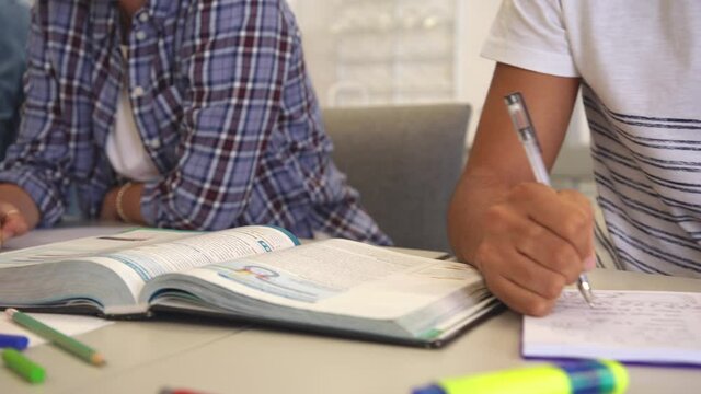 Close up of college students hands on desk in classroom writing notes. Closeup of university students hands taking notes from textbook during lecture. Detail of young woman using pencil on notebook.