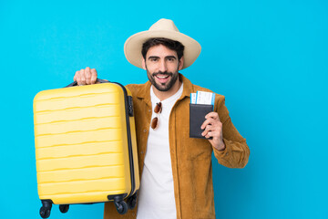Young handsome man with beard over isolated blue background in vacation with suitcase and passport