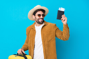 Young handsome man with beard over isolated blue background in vacation with suitcase and passport