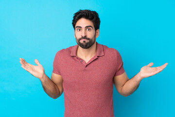 Young handsome man with beard over isolated blue background making doubts gesture