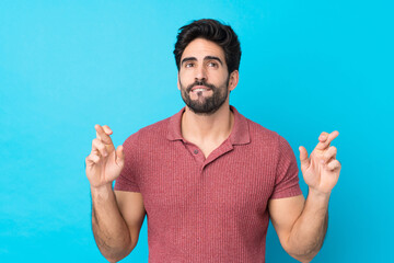 Young handsome man with beard over isolated blue background with fingers crossing and wishing the best