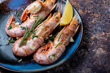 Large cooked shrimps with lemon and rosemary in a plate close-up. Dark background.