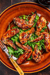 Bbq buffalo chicken wings on a plate with arugula. Dark background. Top view