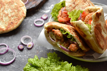 Lavash salad with fried chicken and vegetables. Pita with chicken nuggets, tomatoes, red onions and lettuce and sauce. Healthy fast food. Dark background. Copyspace