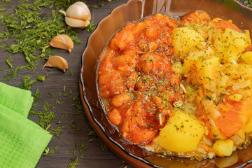 In a glass brown plate there are potatoes with carrots and beans in tomato sauce