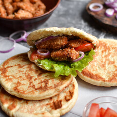 Lavash salad with fried chicken and vegetables. Pita with chicken nuggets, tomatoes, red onions and lettuce and sauce. Healthy fast food. Dark background.
