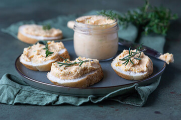 Sandwiches with smoked salmon and soft cream cheese pate or mousse with thyme and rosemary on a ceramic plate, green concrete background.