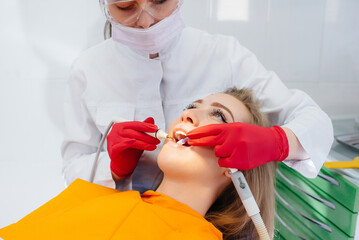 A professional dentist performs treatment and examination of the patient's oral cavity in close-up....