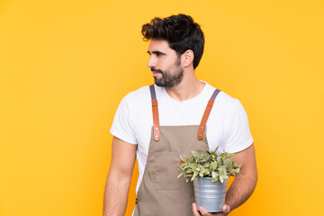 Gardener man with beard over isolated yellow background looking side