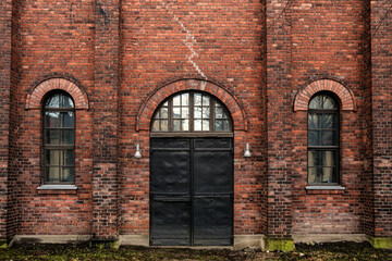 Fototapeta na wymiar Wall of red bricks and old metal industrial doors. An old abandoned warehouse in Turku, Finland.
