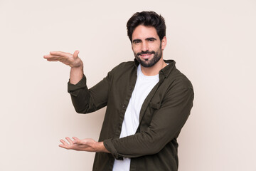 Young handsome man with beard over isolated background holding copyspace to insert an ad
