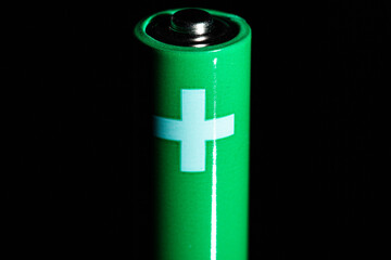 Green tiny double AA battery isolated on a black background with white positive cross