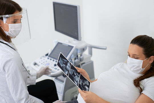 Pregnant woman in face mask looking at ultrasound images