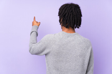 Young african american man isolated on purple background pointing back with the index finger