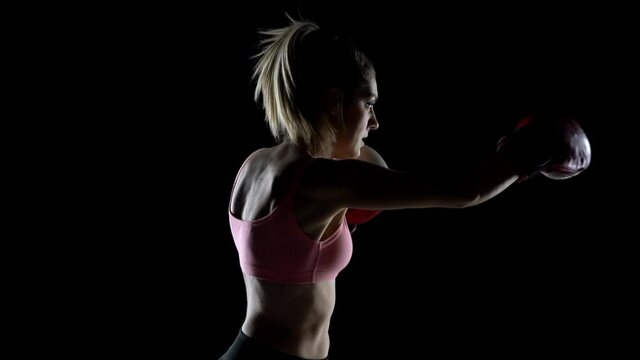 slow motion of the silhouette of a young woman training with boxing gloves. profile view on black background