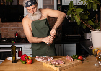 Bearded senior Man cooking meat steak on kitchen.