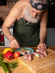 Bearded senior Man cooking meat steak on kitchen.