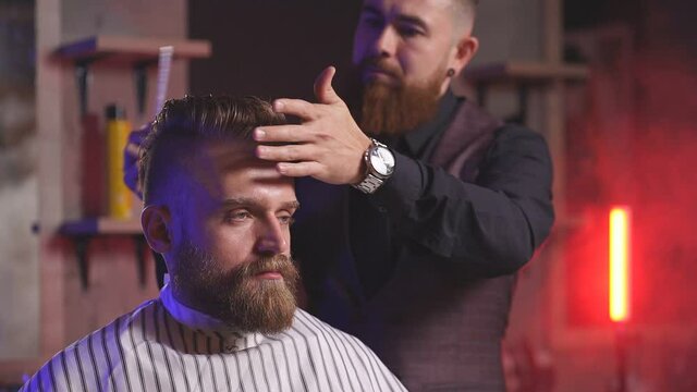 Master cuts hair and beard of men in the barbershop, hairdresser makes hairstyle for a stylish man.