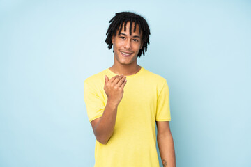 Young african american man isolated on blue background inviting to come with hand. Happy that you...
