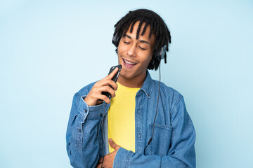 Young african american man isolated on blue background listening music with a mobile and singing