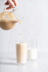 Dalgon brown coffee mixture is poured from the decanter into a glass of milk. Milkshake with instant coffee and sugar, whipped until thick foam.