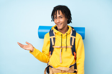 Young mountaineer african american man with a big backpack isolated on a blue background holding...