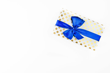 A gift wrapped in white paper with gold circles wrapped in a blue ribbon tied in a bow, isolated on...
