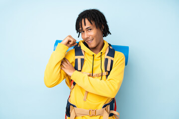 Young mountaineer african american man with a big backpack isolated on a blue background making...