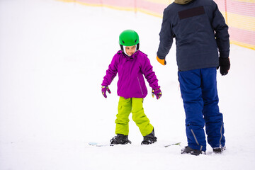 Fototapeta na wymiar Instructors teach a child on a snow slope to snowboard