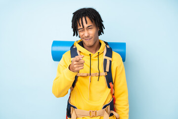 Young mountaineer african american man with a big backpack isolated on a blue background points finger at you