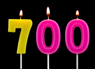 Burning birthday candles isolated on black background, number 700